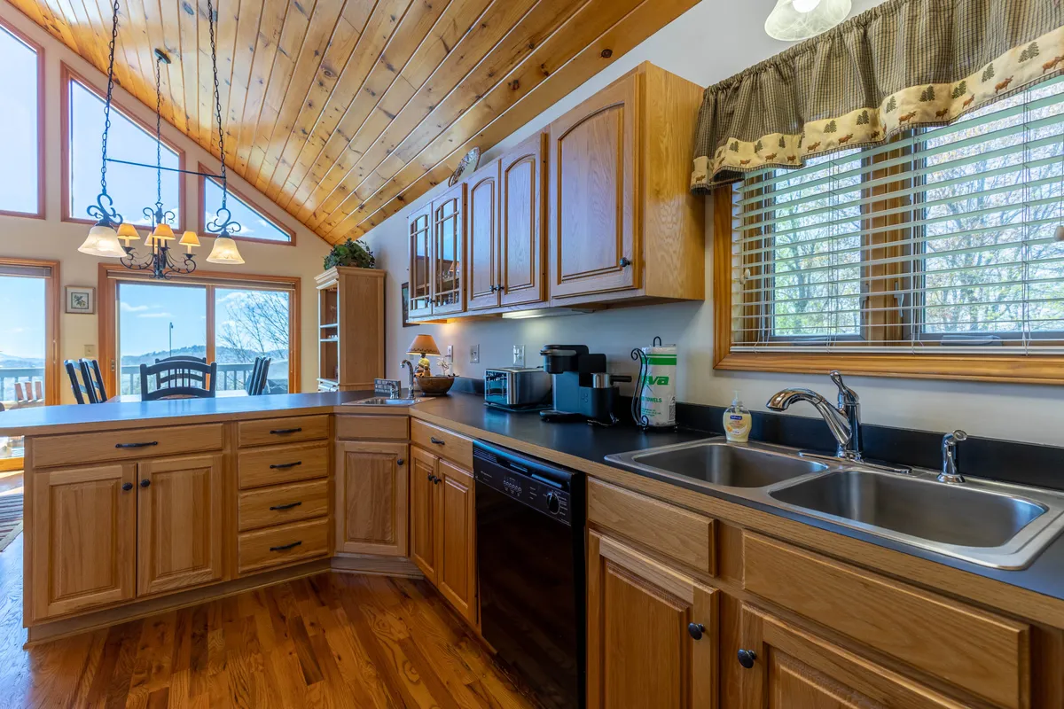 A spacious, open kitchen with a large island ideal for meal preparation and gathering. The area is filled with natural light from generous windows, features warm wooden cabinetry, and is anchored by a stylish chandelier. The setting is cozy and inviting, perfect for group cooking and entertaining.