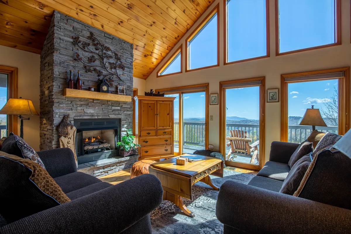 A cozy living space with a rustic stone fireplace, large windows providing mountain views, wooden furniture, and tasteful decorative art. The room beckons families to gather for movie marathons, fireside chats, or relaxed evenings together.