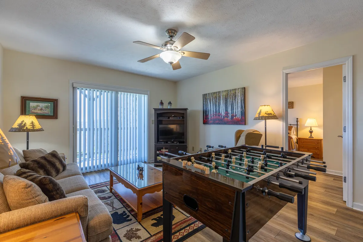 A cheerful family room featuring a foosball table, plush sofa, sliding glass door, and artwork. The setup encourages playful interaction and easy movement between indoor and outdoor spaces, matching the section's emphasis on versatility. The lighting makes the room feel welcoming and active.