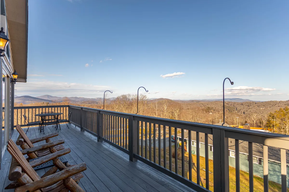 A tranquil outdoor porch with comfy seating and a table overlooking expansive mountain views. The scene is bathed in natural light, suggesting opportunities for relaxing after a day of hiking, or stargazing at night.