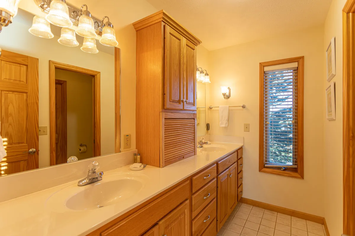 A serene bathroom with dual sinks set in wood cabinetry, bathed in soft natural light from a window. The clean, calming design supports peaceful morning and evening routines.