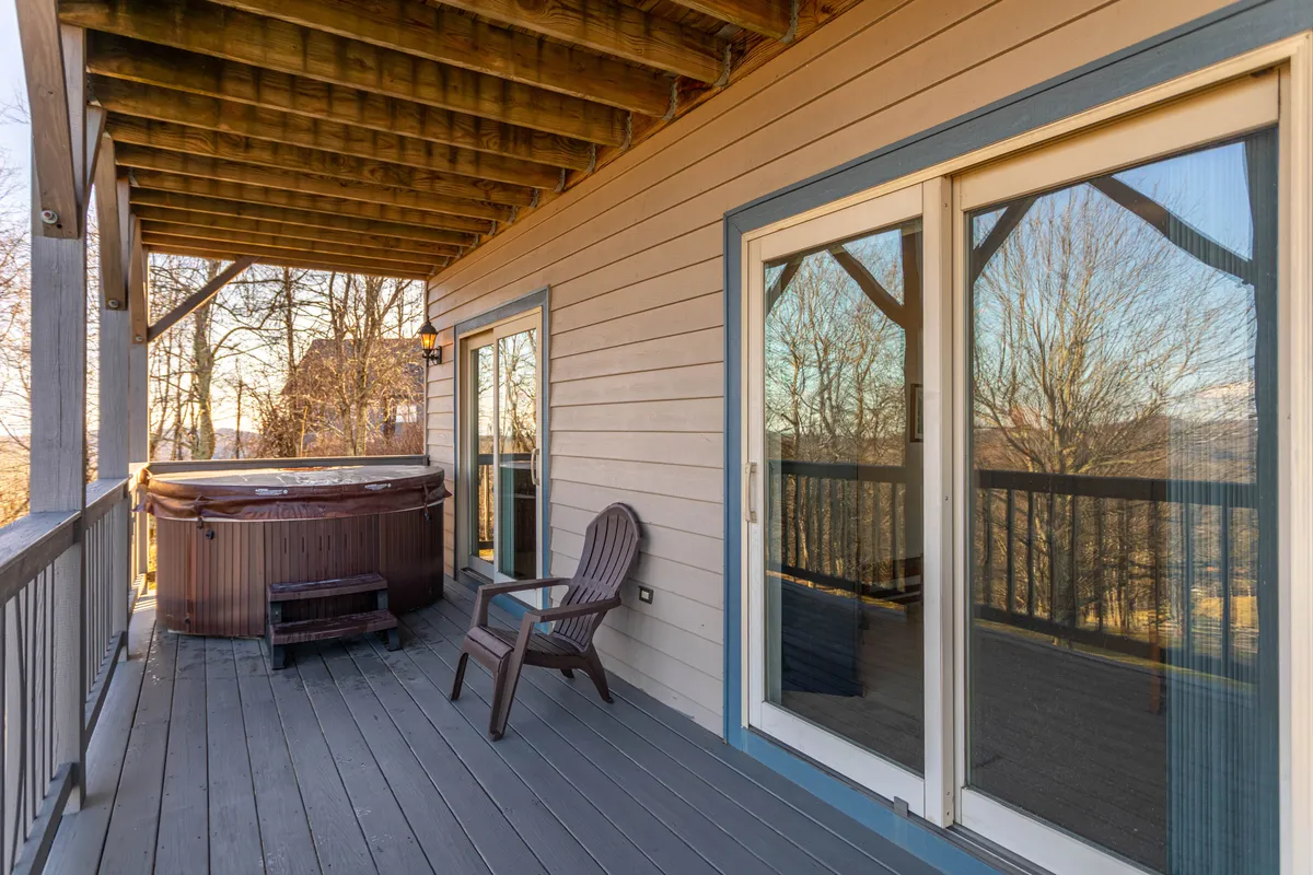 An inviting exterior deck featuring a hot tub, wooden chair, and sliding glass doors that connect the indoor living space to outdoor serenity. The view from the deck hints at nature and sky, suggesting an ideal spot for stargazing or sipping morning coffee together.