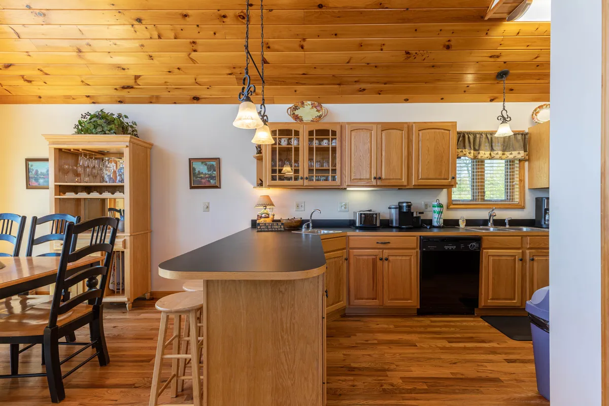 This image offers a focused look at the kitchen and dining area. A large kitchen island sits at the center, surrounded by wooden cabinets and hanging light fixtures. Nearby, a sizeable dining table is positioned by large windows, creating a warm, welcoming space for shared meals and entertaining.