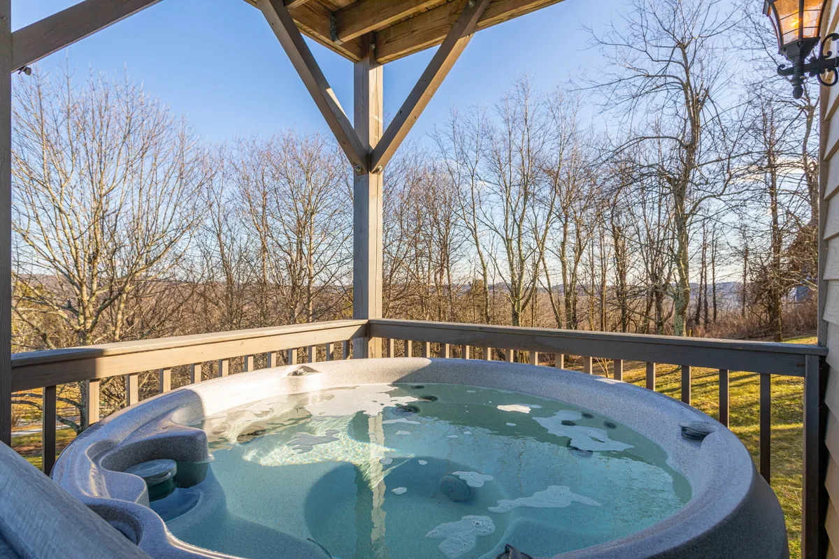This exterior image features a hot tub set on a deck, surrounded by natural greenery and with a beautiful, distant landscape visible beyond. The setup suggests a space for relaxation and socializing outdoors, ideal for families unwinding together after a day of adventure.