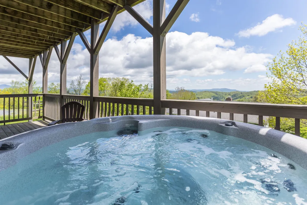 An outdoor deck with a bubbling hot tub overlooking scenic mountain vistas. The serene setting invites relaxation and socializing outdoors, capturing the promise of soaking while enjoying beautiful views. The wooden deck and open sky suggest privacy and the allure of unwinding under the stars.