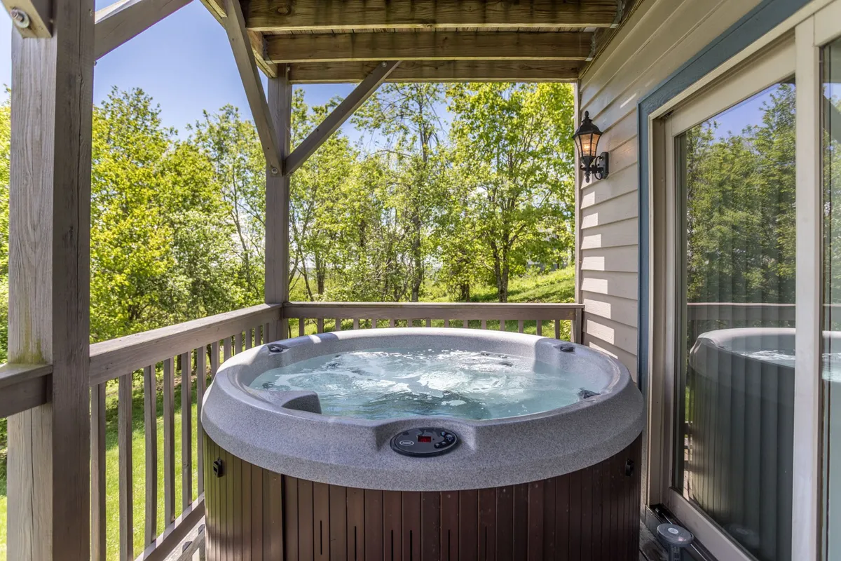 This image shows a tranquil outdoor hot tub set on a deck, surrounded by lush greenery. The hot tub overlooks a scenic natural landscape, inviting guests to unwind while being immersed in nature. The setting evokes a sense of peaceful seclusion, perfect for couples seeking relaxation and romance.